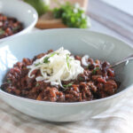 a picture of a blue serving bowl filled with cooked chili topped with cheddar cheese