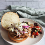 a picture of pulled pork for two on a kaiser bun with coleslaw and a bean salad on the side