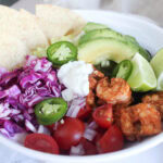 a picture of an assembled shrimp taco bowl with tomatoes, jalapenos and avocado slices on top