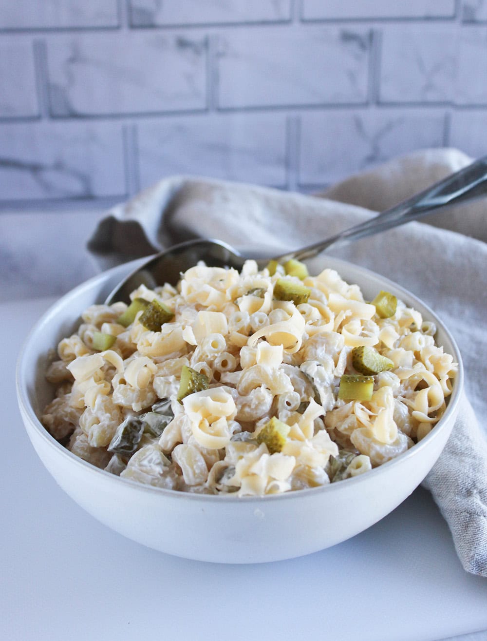 macaroni salad in a white bowl with a serving spoon