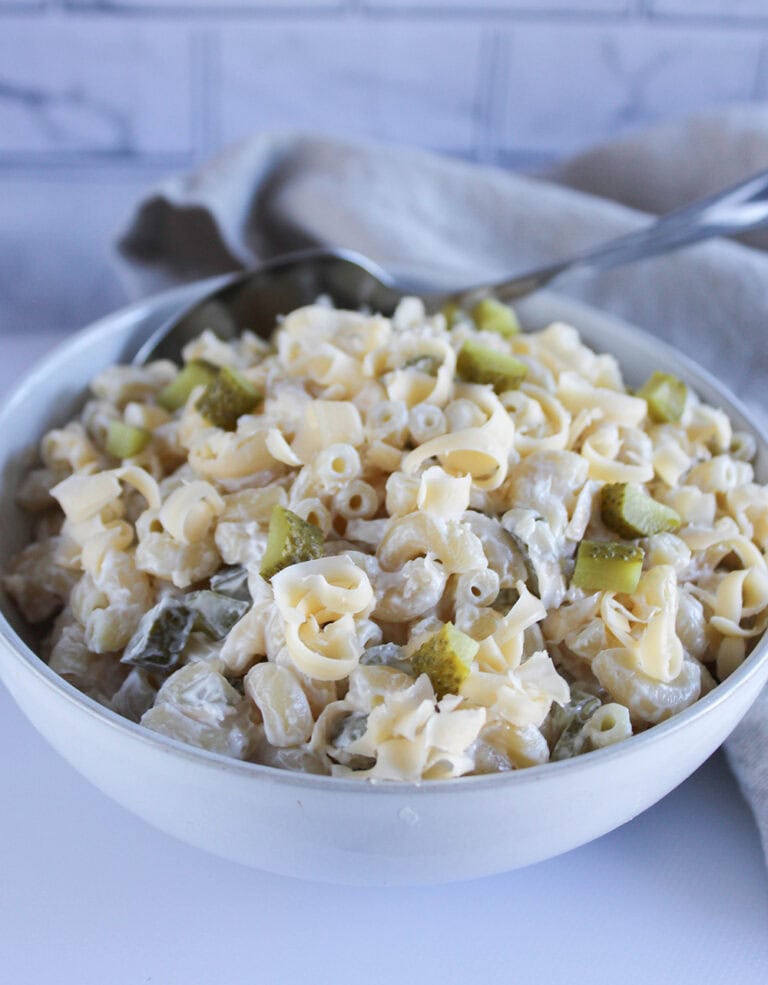 Macaroni salad piled in a white bowl with a serving spoon in the bowl