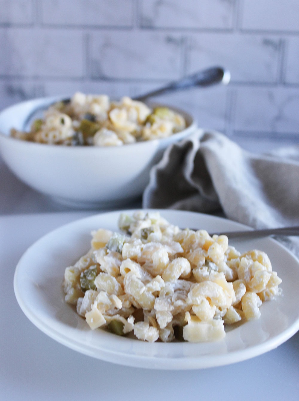 macaroni and cheese salad on a white plate with a serving bowl of mac n cheese salad in the background