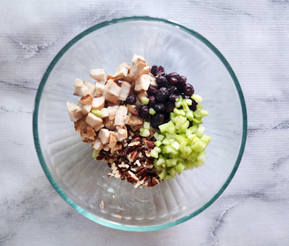 Process step 1 for cape cod chicken salad;  ingredients in a glass bowl with a wooden spoon