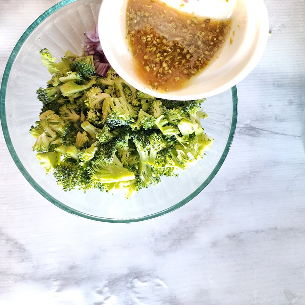 broccoli salad ingredients in a with the dressing pouring in