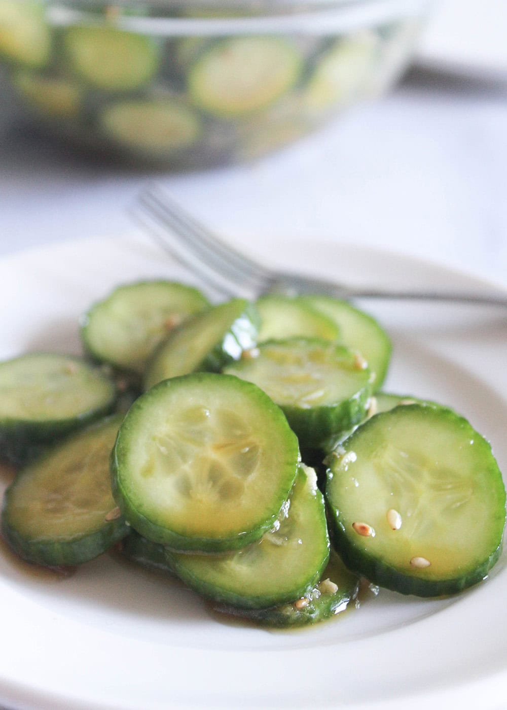 sliced asian cucumber salad in a white plate with a fork on the side