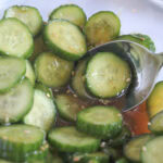 sliced cucumbers in an asian dressing in a glass bowl with a spoon in the bowl