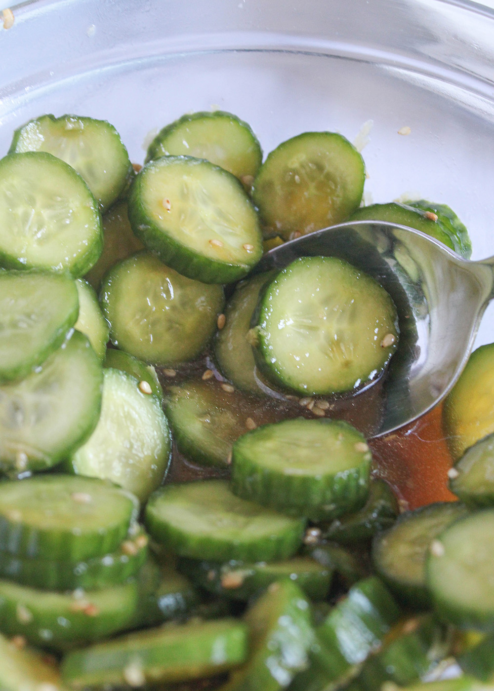 sliced cucumbers in an asian dressing in a glass bowl with a spoon in the bowl