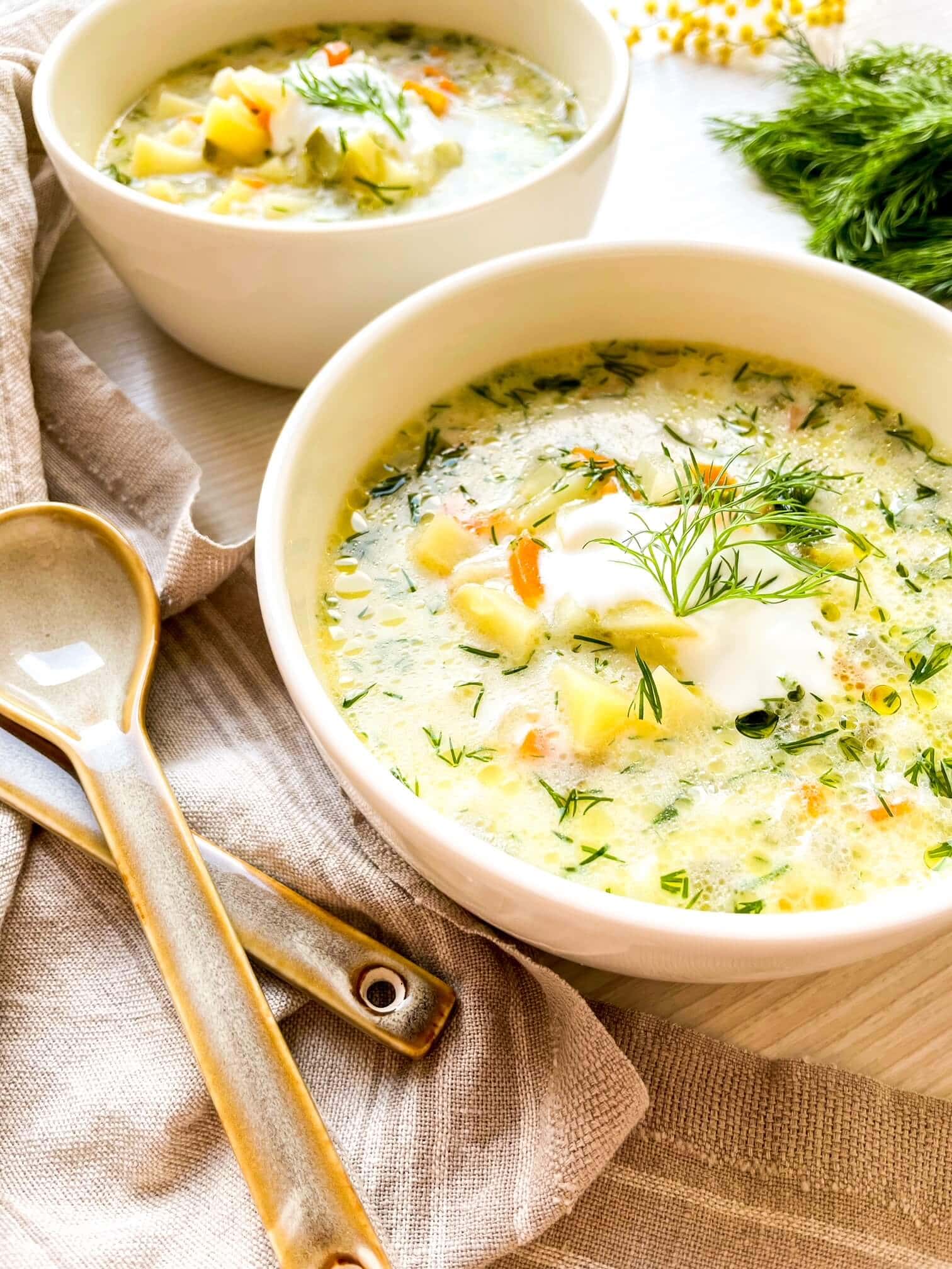 dill pickle and potato soup in a shite serving bowl garnished with fresh dill